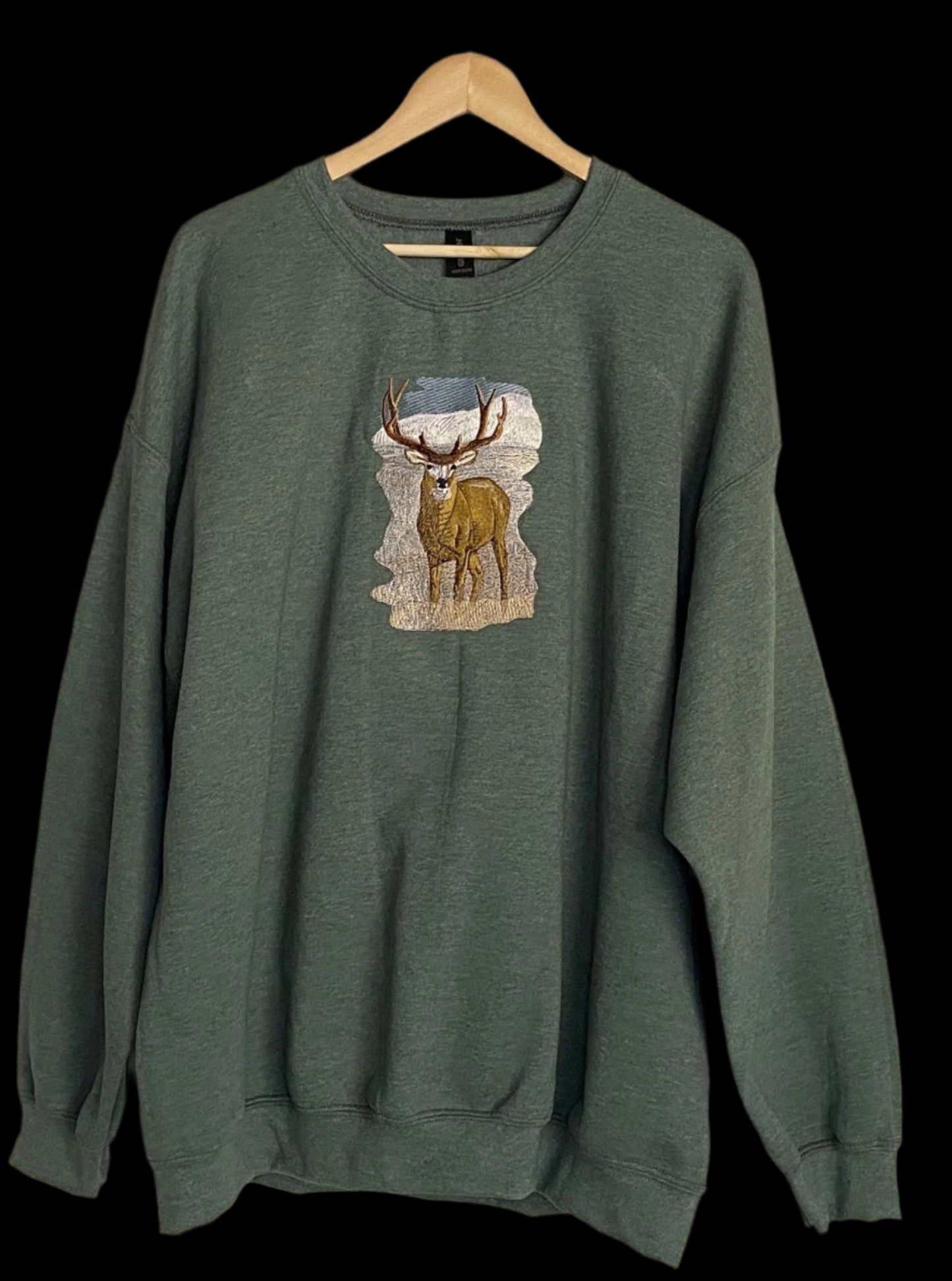 Green sweatshirt with a deer graphic on a hanger against a beige wall