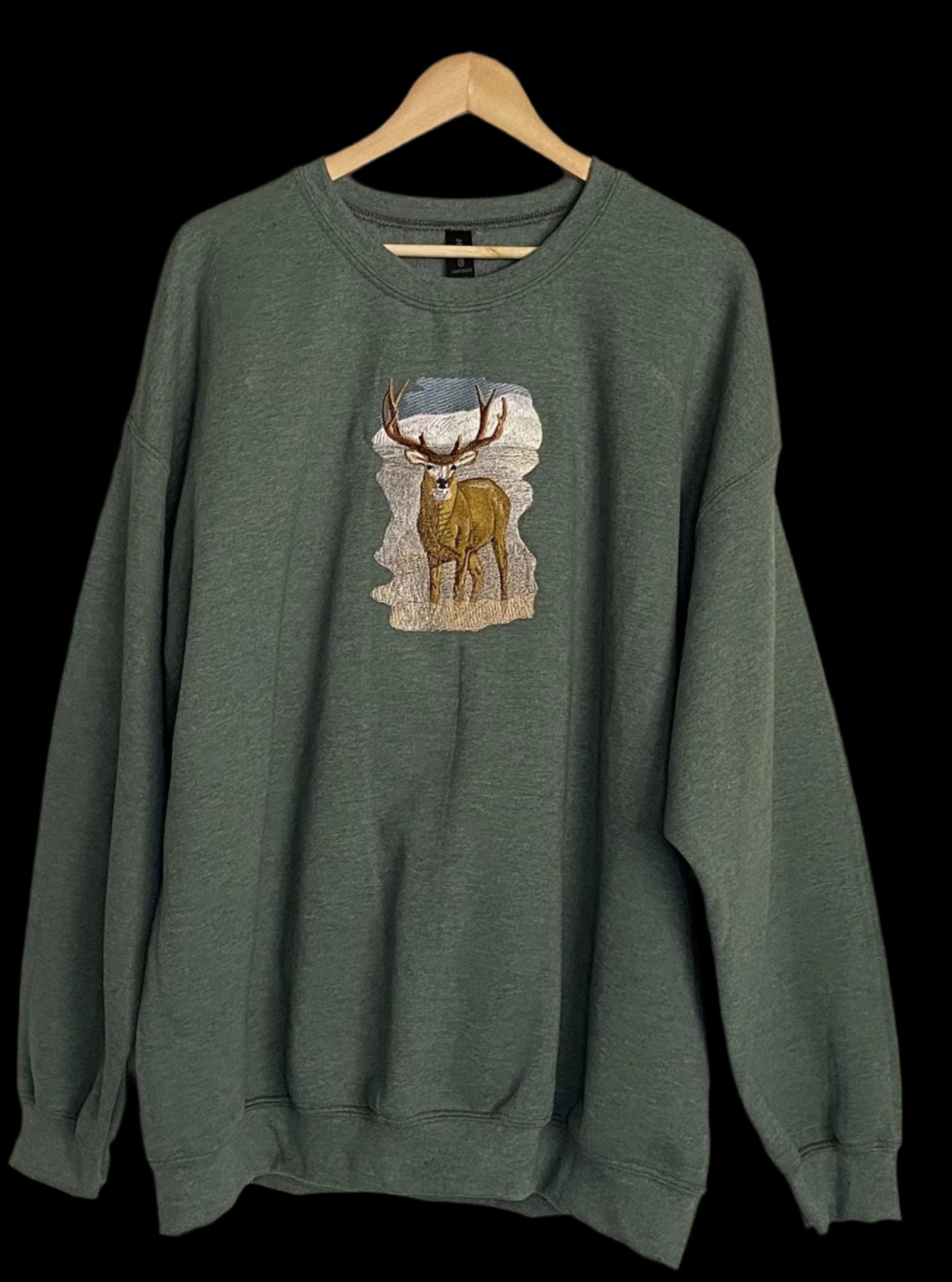 Green sweatshirt with a deer graphic on a hanger against a beige wall