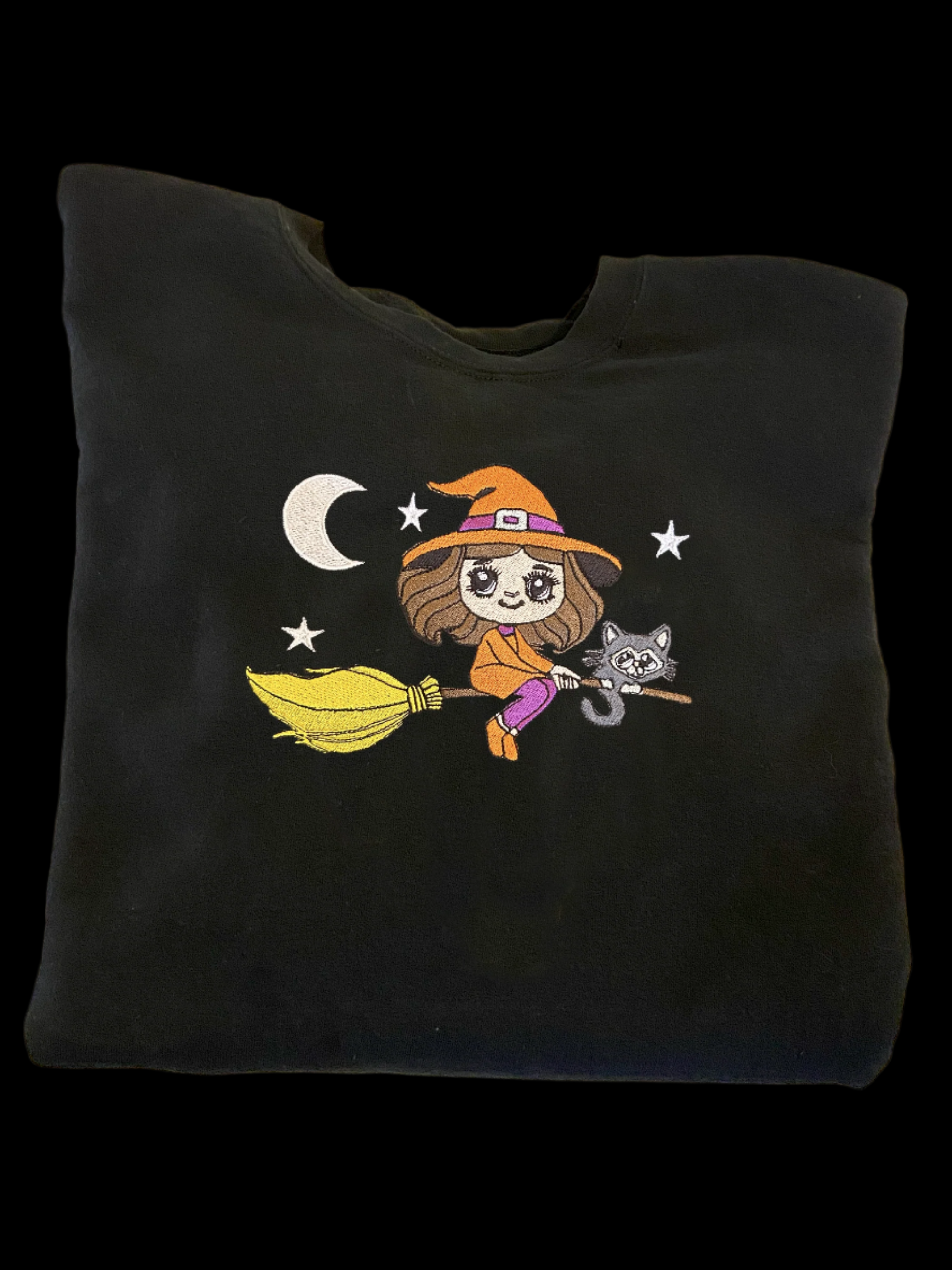 Black sweatshirt with a cartoon witch design on a white surface